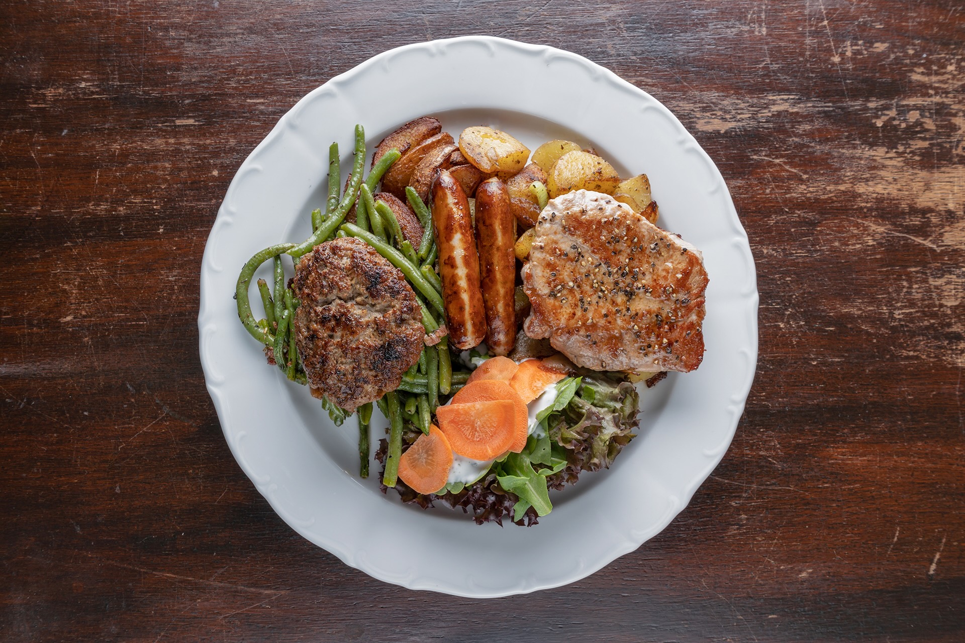 Gemischter Teller mit Boulette, Schweinesteak, Bratwürsten, Bratkartoffeln, Bohnen und Salat